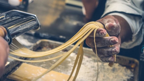 Hoogwaardige pasta maken in een professionele keuken met een hand die pasta uit de machine haalt.