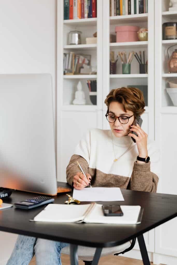 Efficiënte zakenvrouw aan het werk met telefoon, notities en laptop in een moderne kantooromgeving voor zakelijke groei en ondernemerschap.